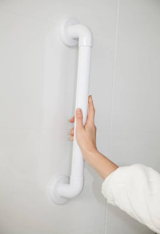 Hand holding a white fluted grab rail on a tiled wall.