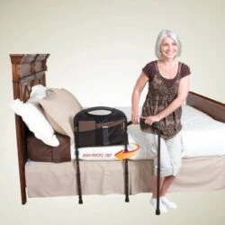 Woman using a mobility bed rail with a swing-out arm next to a wooden bed.