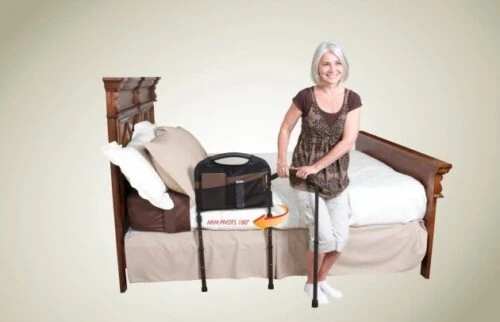 Woman using a mobility bed rail with a swing-out arm next to a wooden bed.