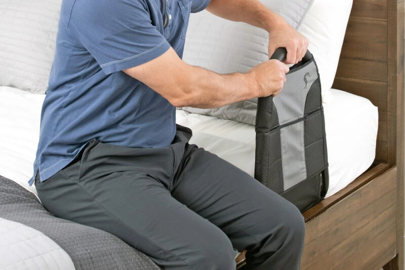 Man holding the handle of a Stander Bedside Econorail attached to a bed.