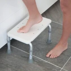Person using a white bath step with adjustable legs in a bathroom.