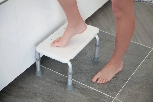 Person using a white bath step with adjustable legs in a bathroom.
