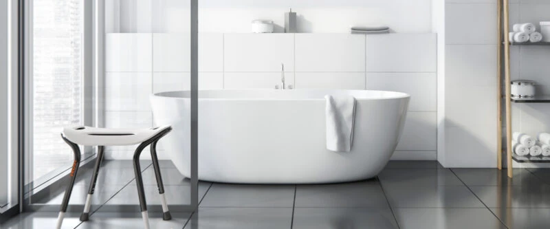 White bath stool with black legs next to a bathtub in a modern bathroom.