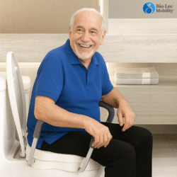Elderly man sitting on a raised toilet seat with handles in a bathroom.