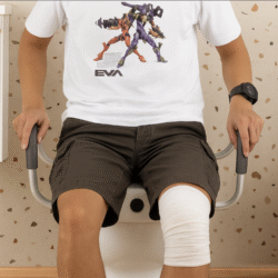 Person sitting on a toilet with raised seat and foam handles.