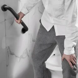 Person using a bathroom safety handle mounted on a tiled wall.