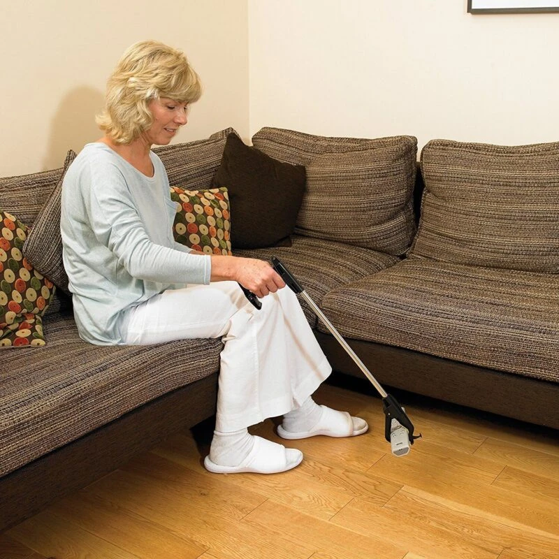 Person using a long reach grabber tool while sitting on a couch.