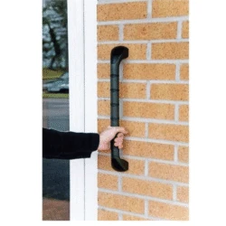 Hand holding a black safety handle mounted on a brick wall.