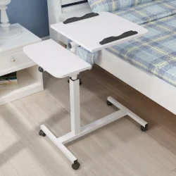 White overbed table with adjustable height next to a bed.