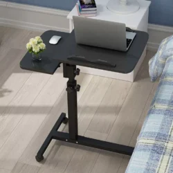 Black overbed table with a laptop and mouse beside a bed.