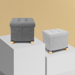 Two pouffe stools with storage in light and dark grey on display blocks.
