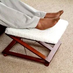 Person resting feet on a wooden foot stool with a white padded cover.