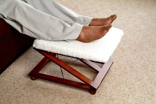 Person resting feet on a wooden foot stool with a white padded cover.