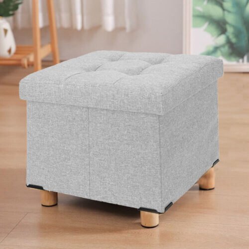 Light grey pouffe stool with wooden legs on a wooden floor.