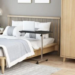Overbed table on wheels with a laptop, positioned by a bed.