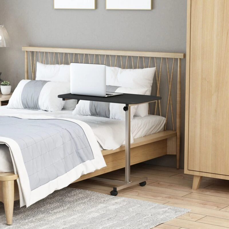 Overbed table on wheels with a laptop, positioned by a bed.