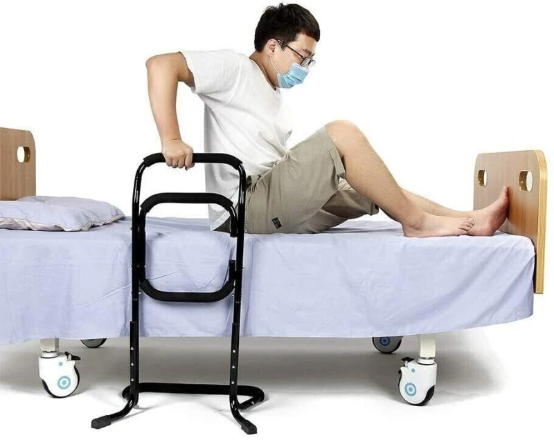 Person using a black standing aid on a bed.