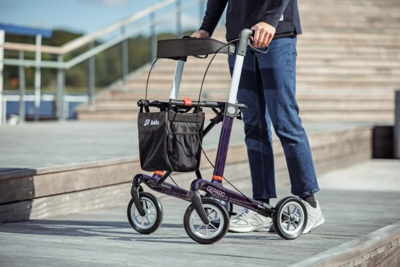 Person using a Gepard rollator outdoors on a wooden deck.