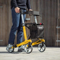 Person using a yellow Gepard rollator outdoors.