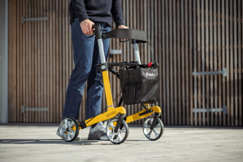 Person using a yellow Gepard rollator outdoors.