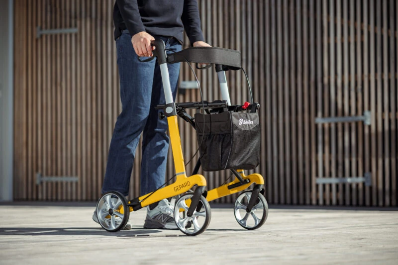 Person using a yellow Gepard rollator outdoors.