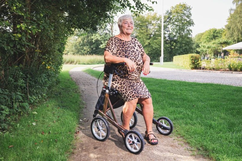 Woman seated on a Mobilex Lion rollator on a path in a park.