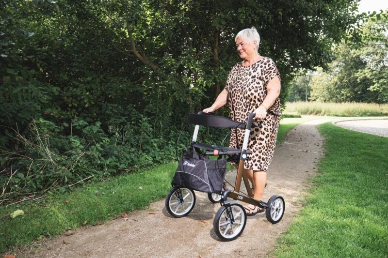 Person using a Mobilex Lion rollator on a gravel path surrounded by greenery.