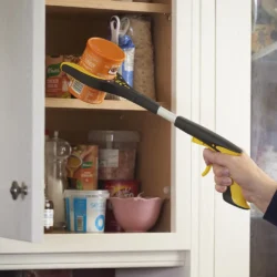 Person using a small grabber tool to reach an orange can from a kitchen cabinet.