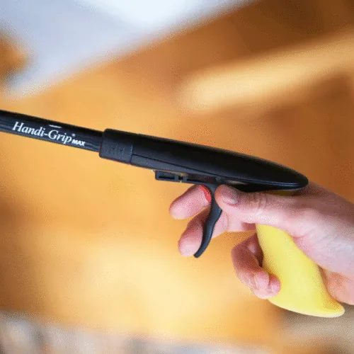Person holding a Handi-Grip MAX reacher with a yellow handle.