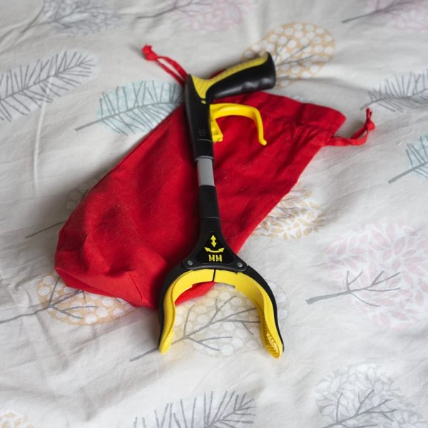 Handi-Grip Mini grabber tool on a bed with a red bag.
