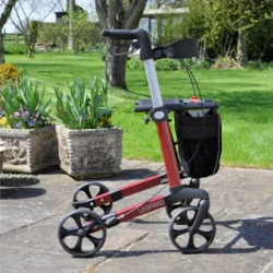 Red rollator walker with black wheels and seat in a garden setting.