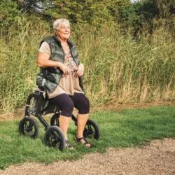 Person sitting on a Mobilex Puma Air rollator on a grassy path.