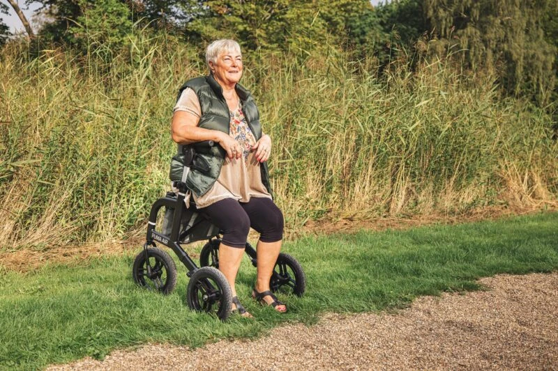 Person sitting on a Mobilex Puma Air rollator on a grassy path.
