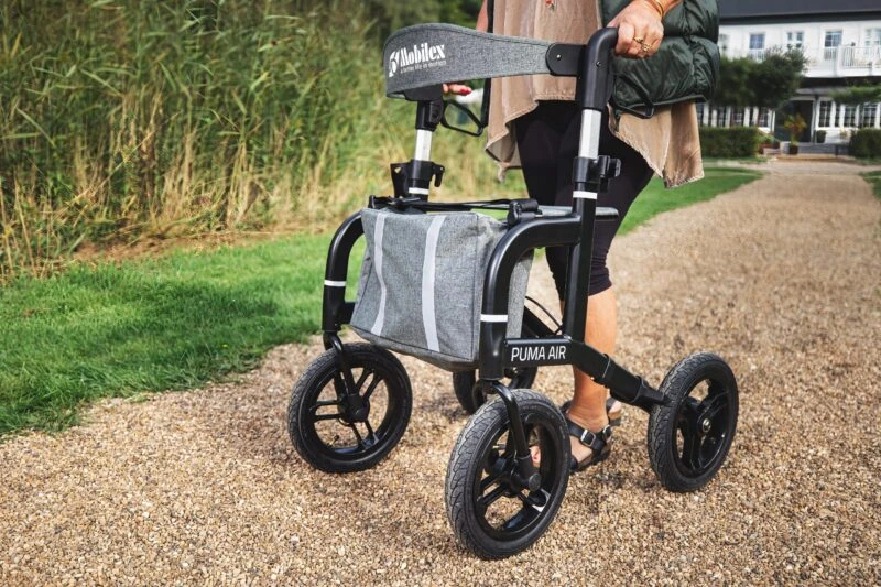 Person using a Mobilex Puma Air rollator on a gravel path.