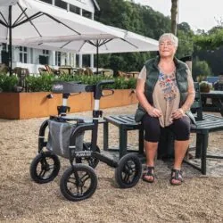 Woman sitting on a bench next to a Mobilex Puma Air rollator with large wheels.