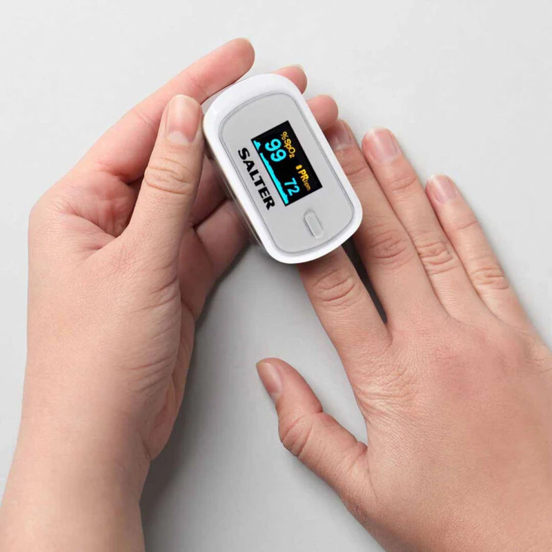 Person using a fingertip pulse oximeter displaying readings.