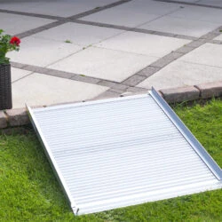 Aluminium rollable ramp placed on grass leading to a paved area.