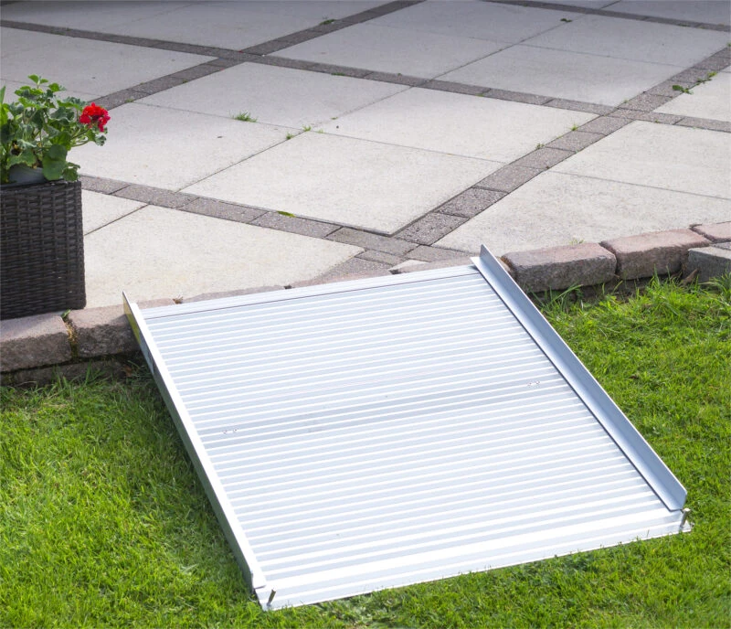 Aluminium rollable ramp placed on grass leading to a paved area.