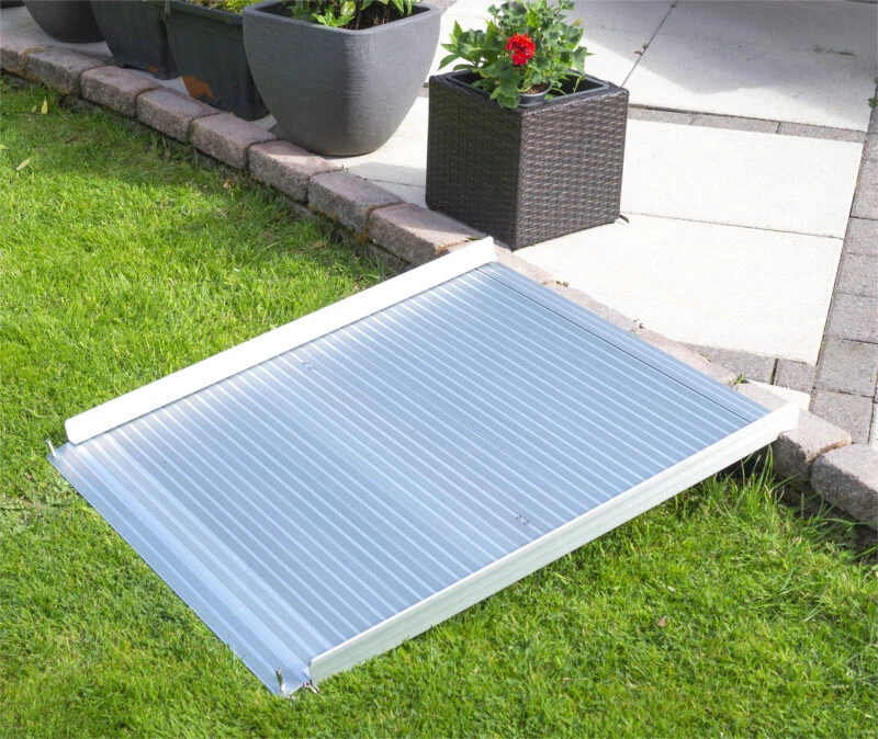 Aluminum rollable ramp placed over a grass and stone step.
