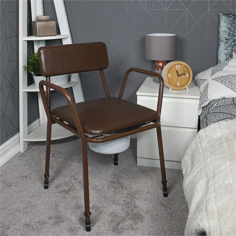Brown commode chair with padded back next to a bedside table and bed.