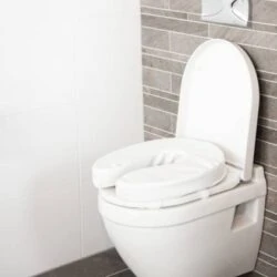 Padded raised toilet seat installed on a white toilet in a modern bathroom.