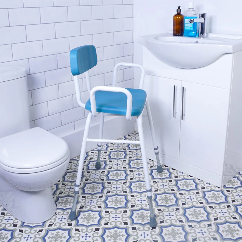 Perching stool with padded back and armrests in a bathroom setting.