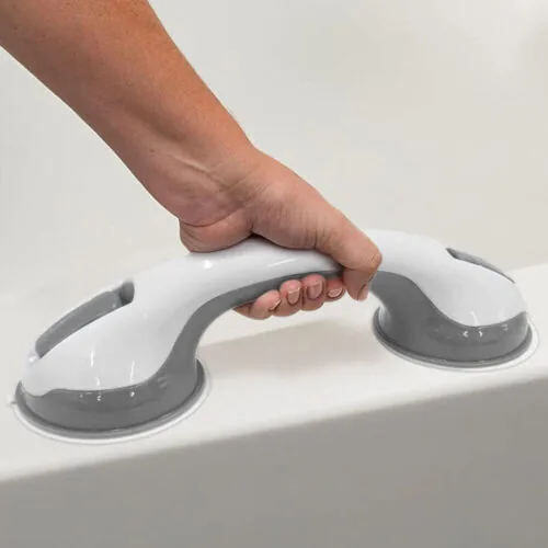 Hand holding a white and grey suction grab bar attached to a smooth surface.