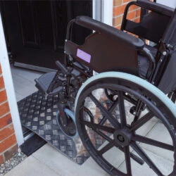 Wheelchair using an aluminium bridge ramp at a doorway.