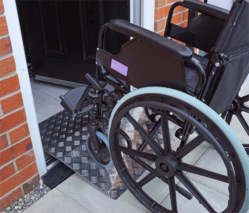 Wheelchair using an aluminium bridge ramp at a doorway.