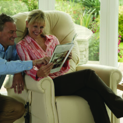 Couple reading in a beige recliner by a sunny window.