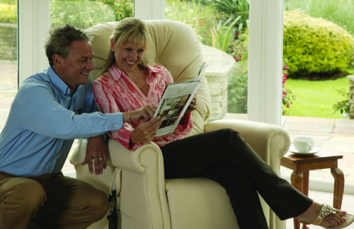 Couple reading in a beige recliner by a sunny window.