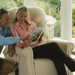 Couple sitting in a cream recliner chair reading a magazine.