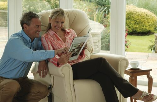 Couple sitting in a cream recliner chair reading a magazine.