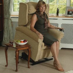 Woman sitting in a beige riser recliner chair next to a small table with fruit.